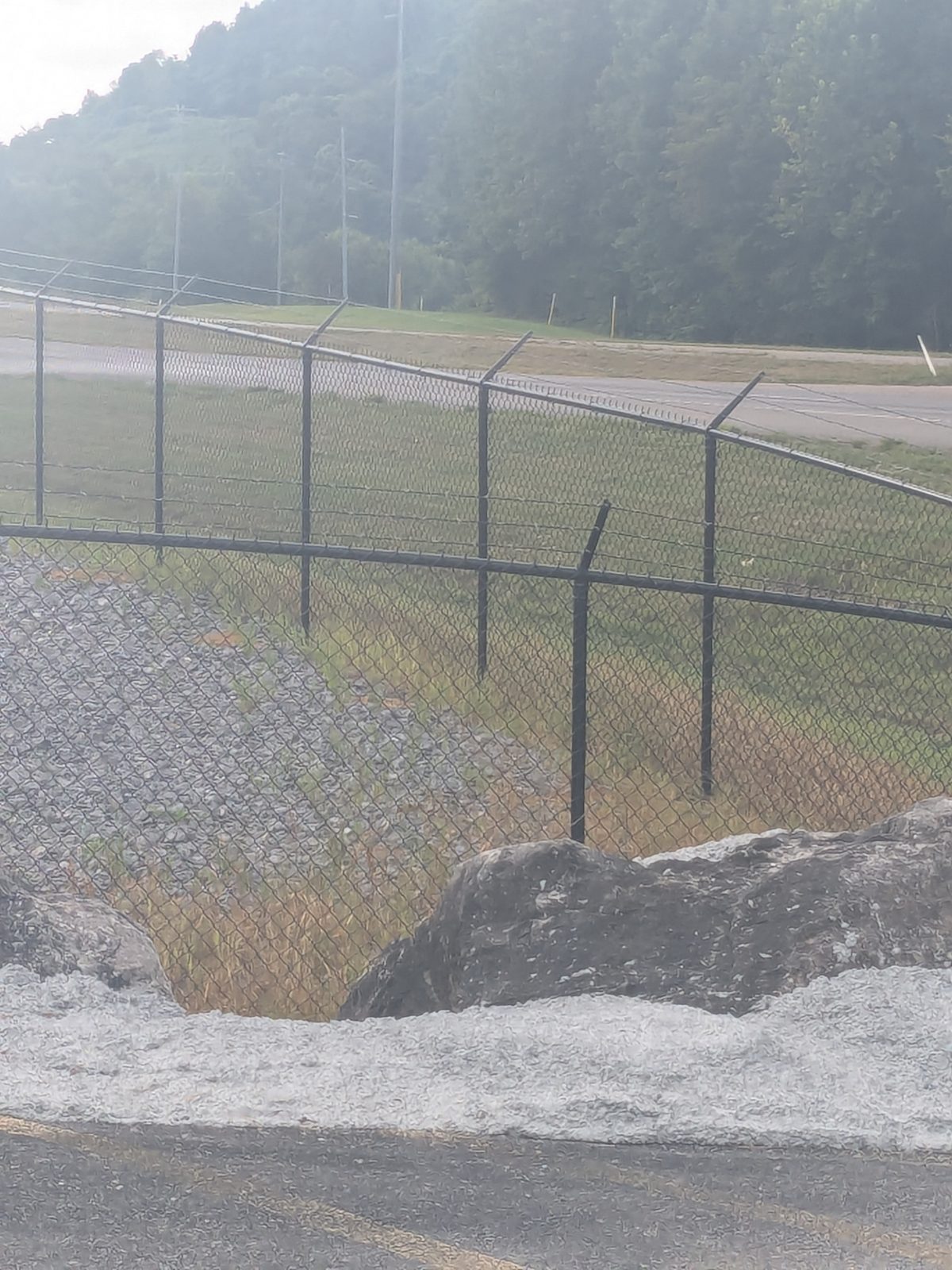 Tall security chain link fence topped with three strands of barbed wire around an industrial yard