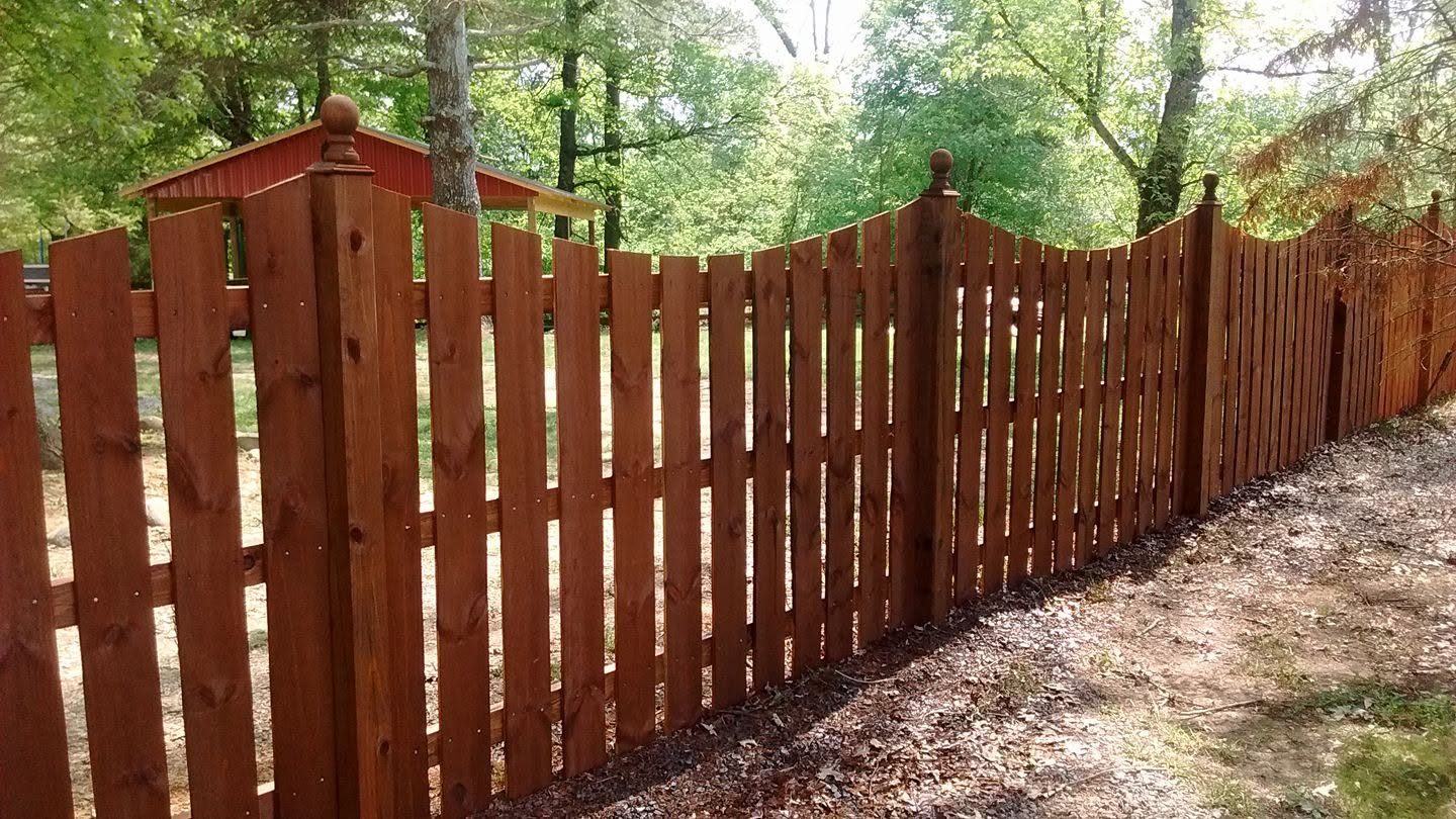 Scalloped-top wood privacy fence with a gently curved upper rail along a property line